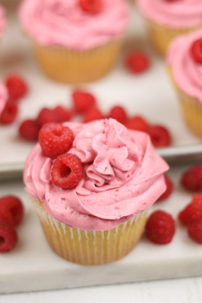lemon cupcakes with raspberry frosting and fresh raspberries on sheet pan