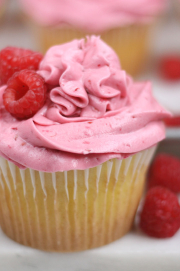 Lemon cupcake with raspberry frosting and fresh raspberries around it