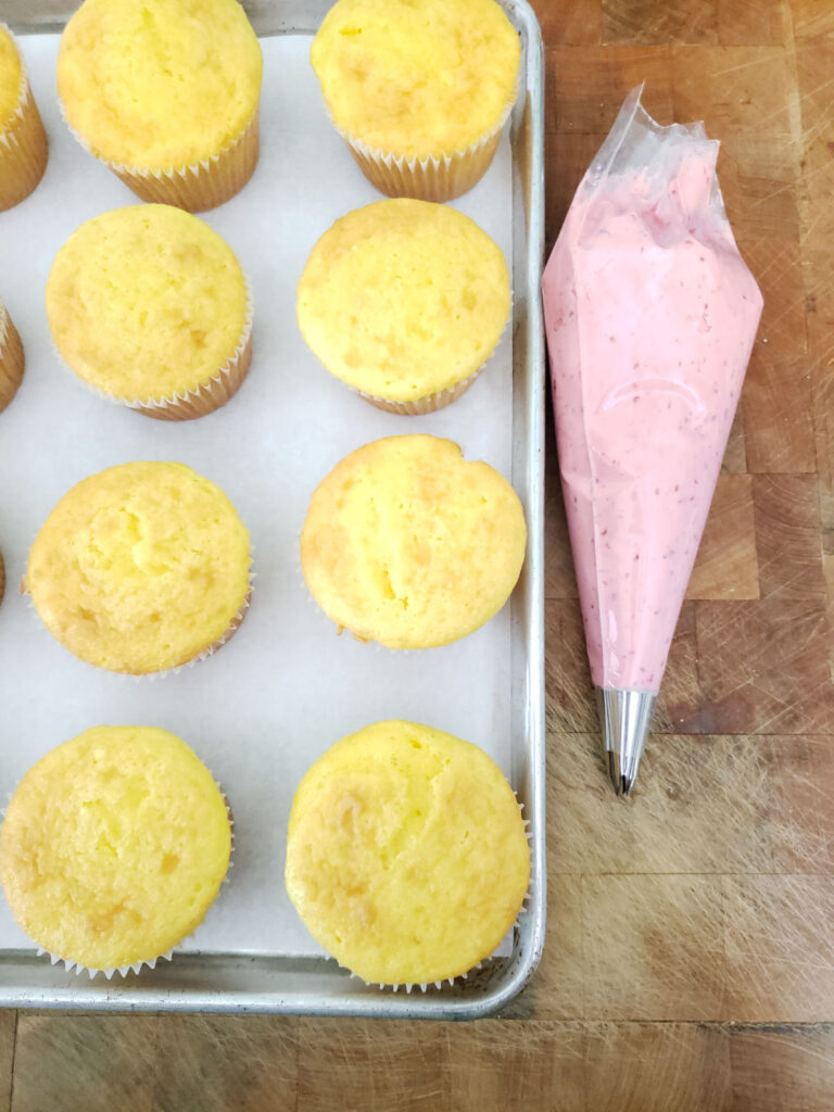 lemon cupcakes on half sheet pan with pastry bag of frosting to the right