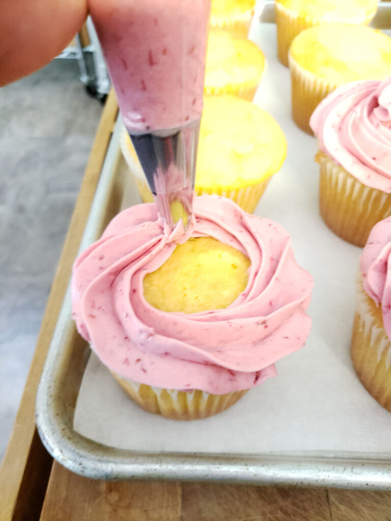 swirling on raspberry frosting on lemon cupcakes with a pastry bag