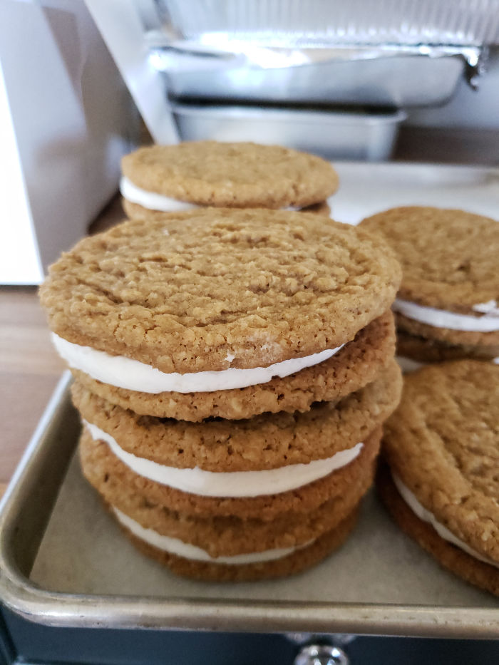 Oatmeal cream sandwich cookies stacked on each other on a half sheet pan lined with white parchment paper.