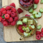 Raspberry rhubarb jam in glass jar with spoon, raspberries and rhubarb pieces in glass Depression glass tea cups