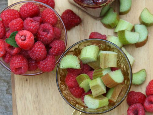 Raspberry rhubarb jam in glass jar with spoon, raspberries and rhubarb pieces in glass Depression glass tea cups