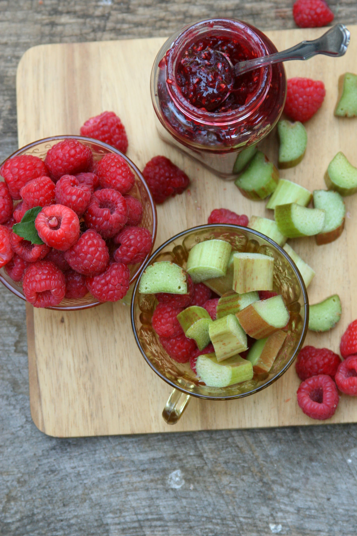 Raspberry rhubarb jam in glass jar with spoon, raspberries and rhubarb pieces in glass Depression glass tea cups.