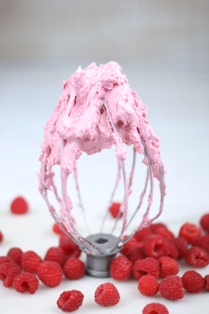 Homemade raspberry frosting on a mixer beater and fresh raspberries around it