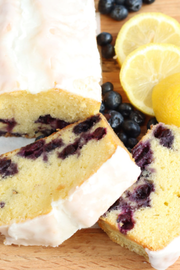 Slices of lemon blueberry bread on wooden cutting board, slices of lemons, fresh blueberries.