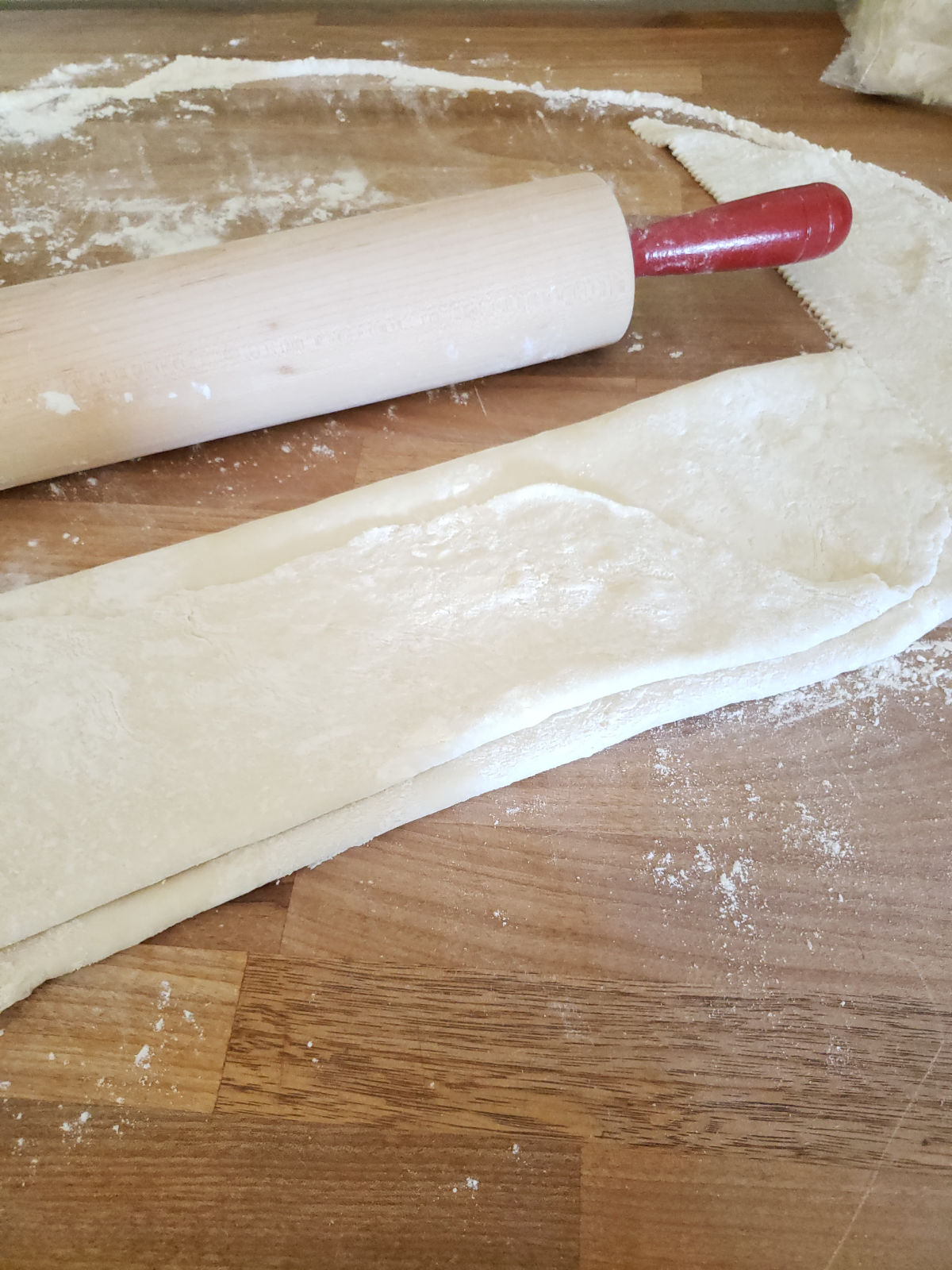 pie crust folded with wooden rolling pin red handles on butcher block.
