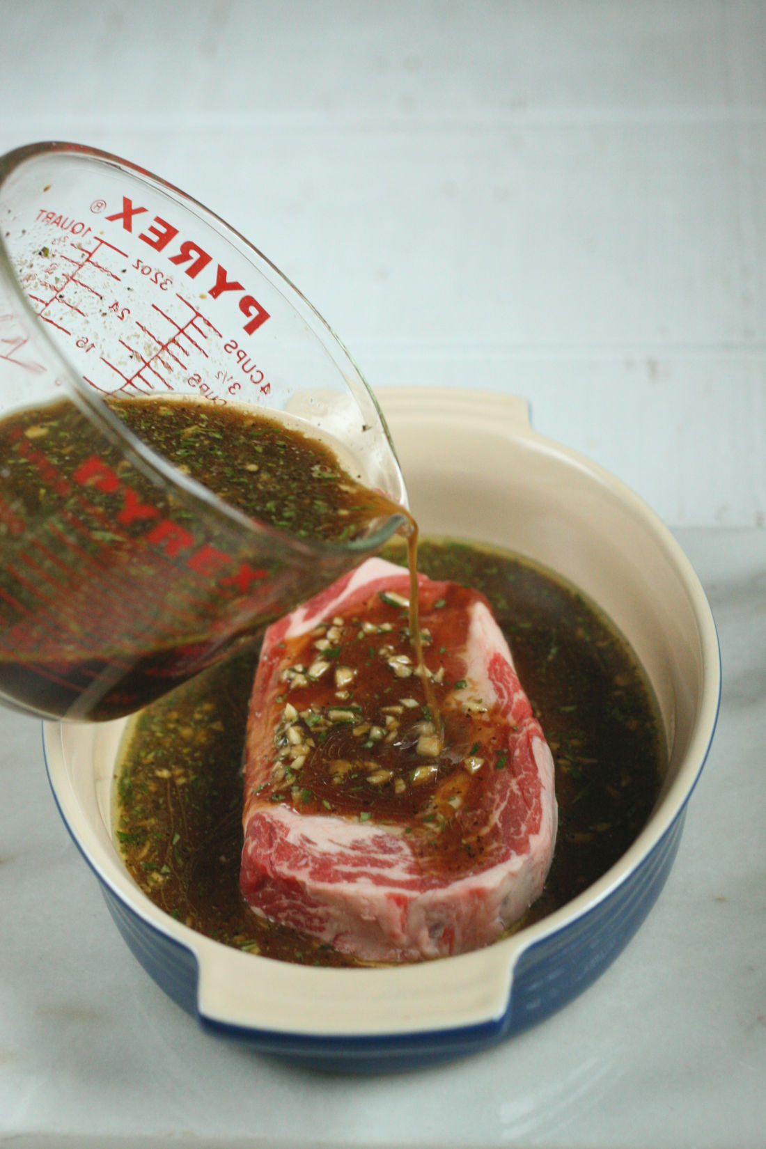 steak marinade in a glass measuring cup being poured over a steak.