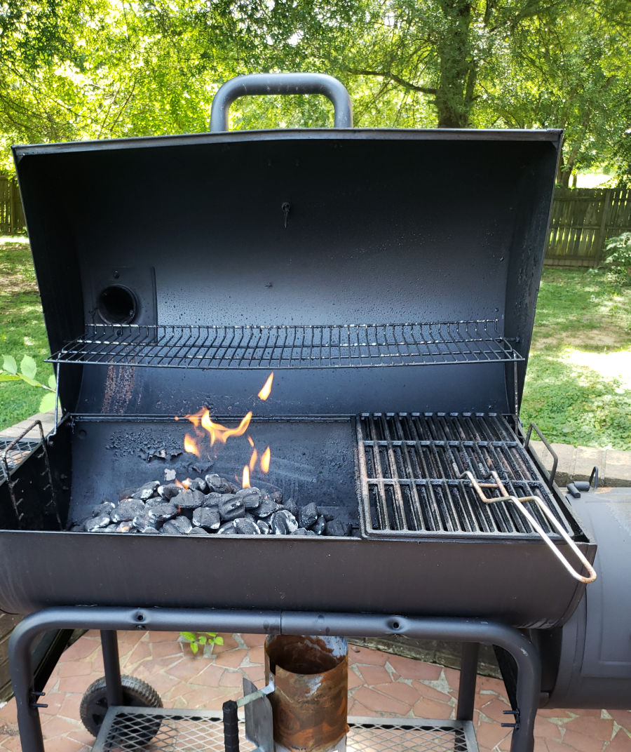 charcoal grill with lid open while charcoal burns with flames.
