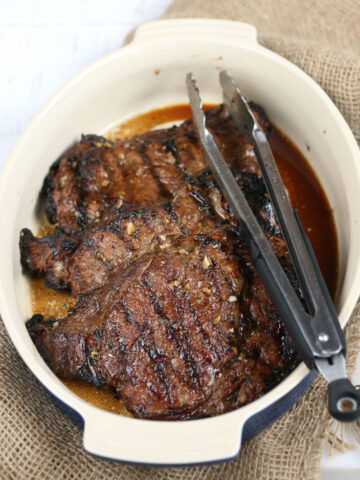 grilled steak in ceramic baking dish with long tongs