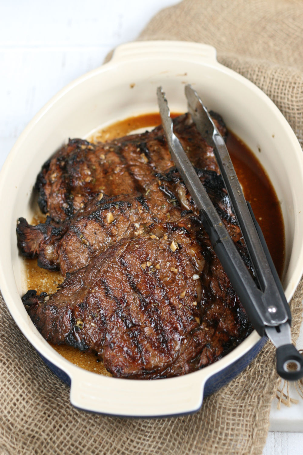 grilled steak in ceramic baking dish with long tongs.