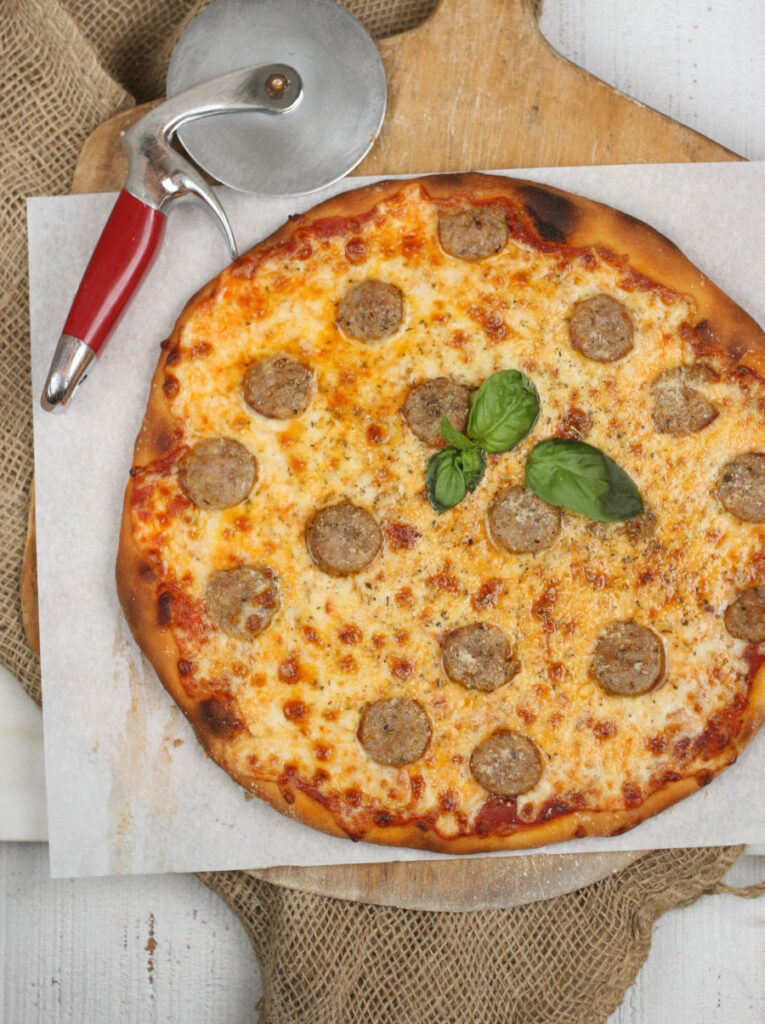 Homemade Italian style pizza with pieces of sweet sausage and basil leaves in the center