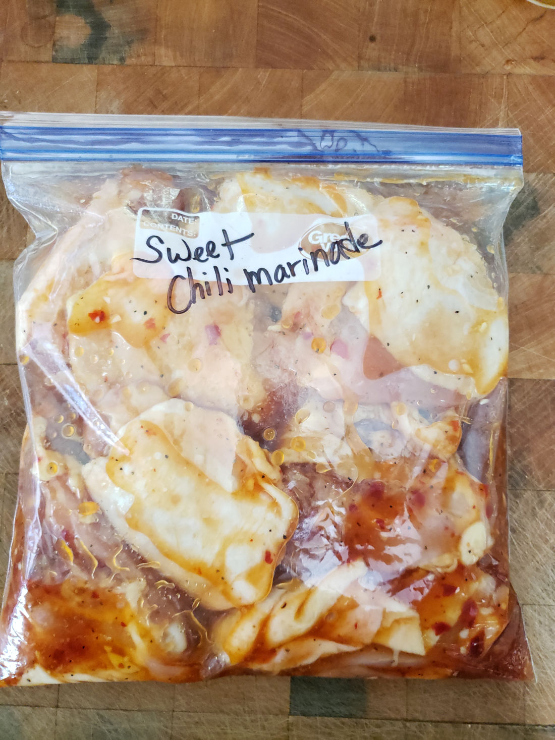chicken marinating in gallon Ziploc bag on butcher block.