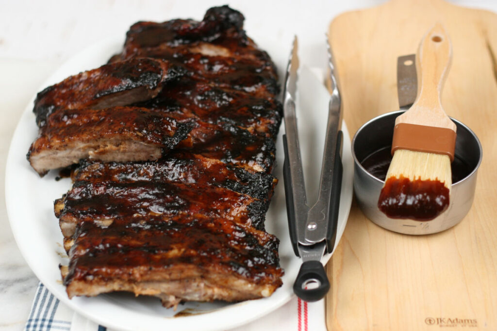 BBQ Pork ribs on a white serving plate with metal tongs