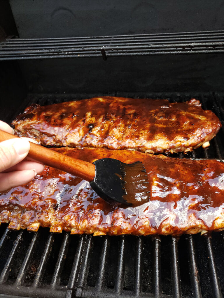 pork spare ribs on grill basting barbecue sauce with brush