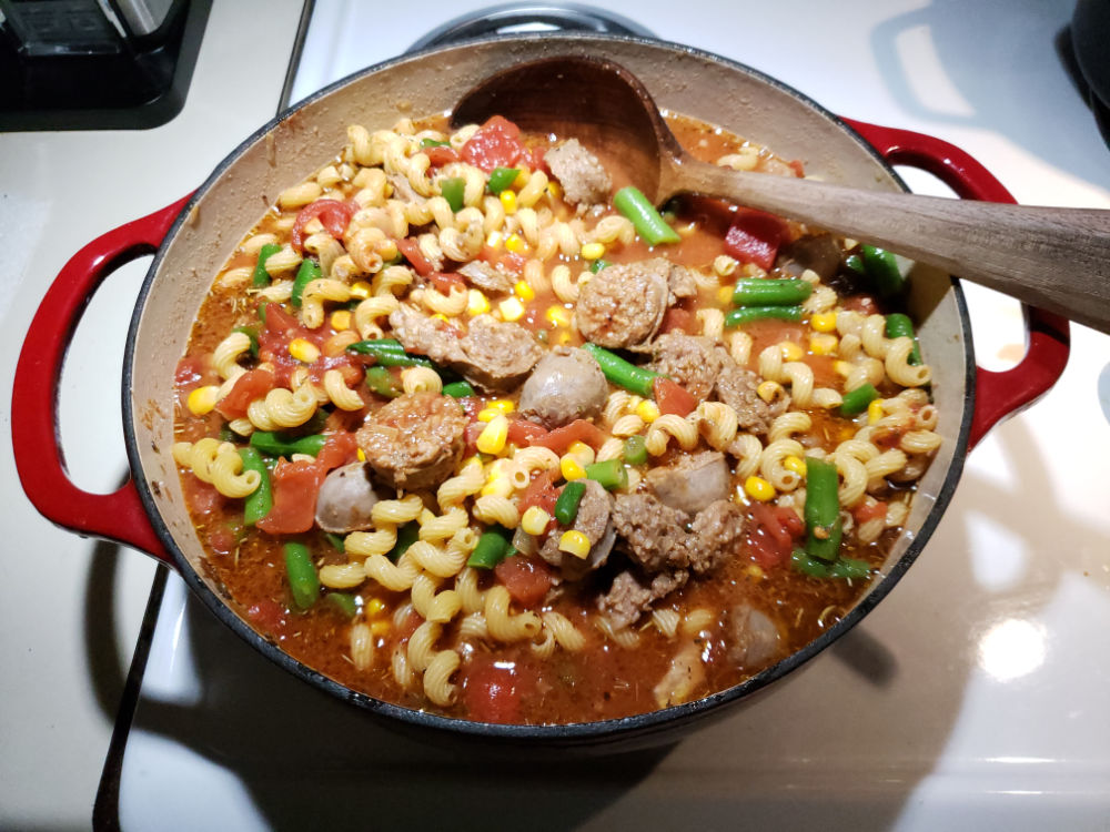 sausage soup with green beans, corn, and pasta in a red Dutch oven on kitchen stove