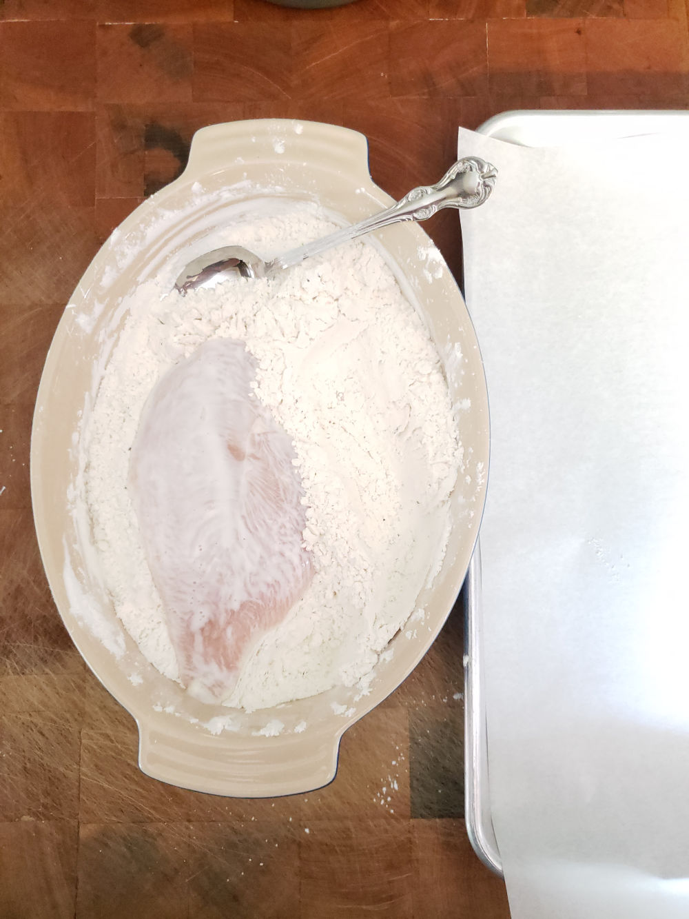 flour and cornstarch mixture in oval ceramic baking dish coating chicken pieces.