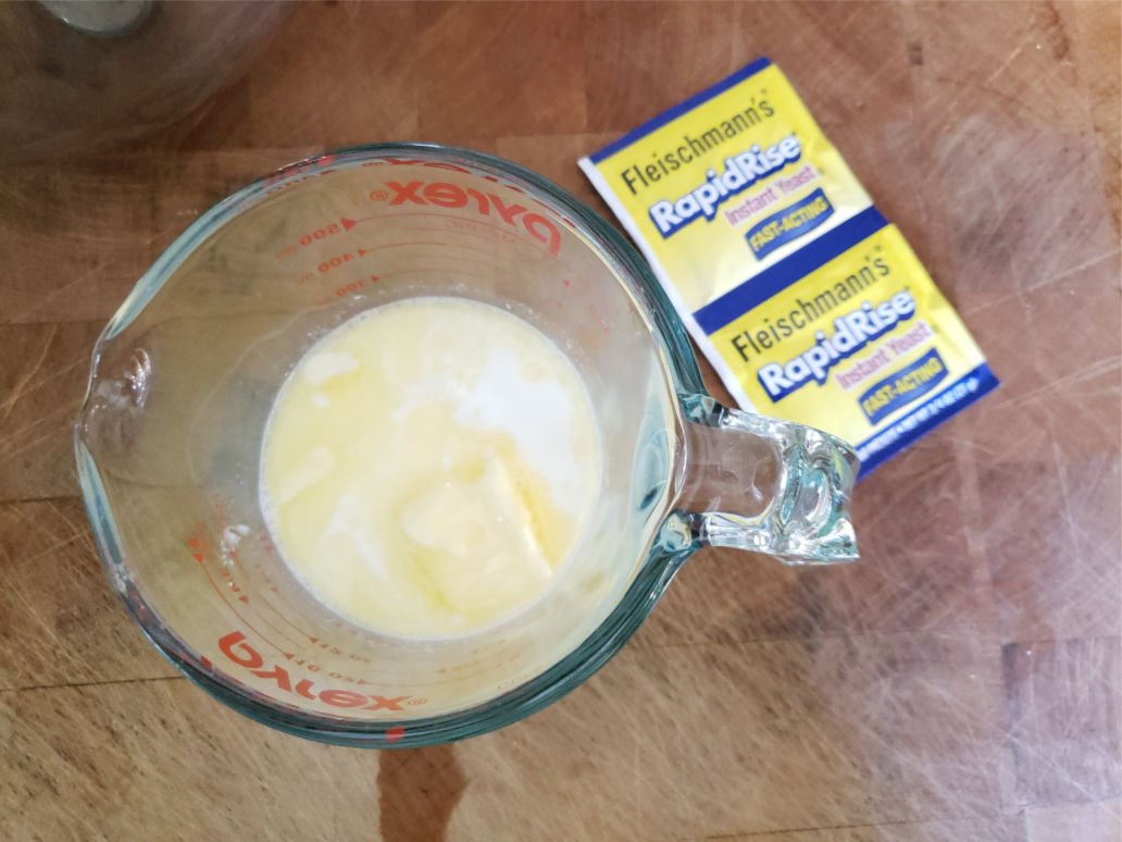 milk, water, and butter in glass measuring cup on butcher block.