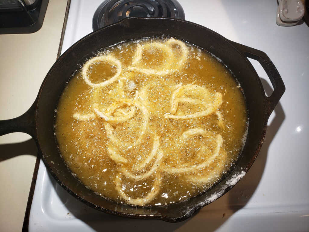 frying buttermilk onion rings in a cast iron skillet on white kitchen stove