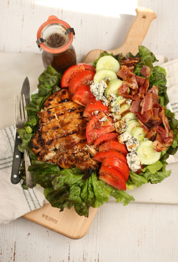 Grilled Chicken, chunks of bacon, sliced tomatoes, cucumbers, and blue cheese on green leaf lettuce on serving plate