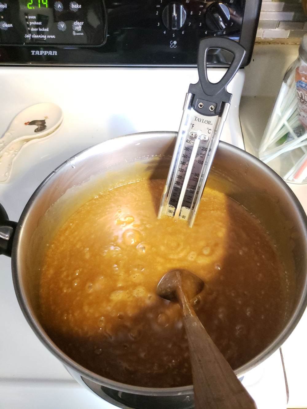 homemade caramel in a pot on a kitchen stove with a candy thermometer in the pot measuring the temperature