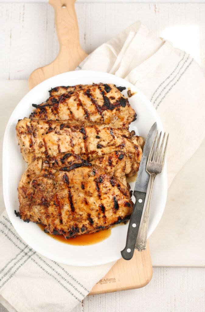 grilled chicken breasts on a white oval serving plate with fork and knife on right side of plate