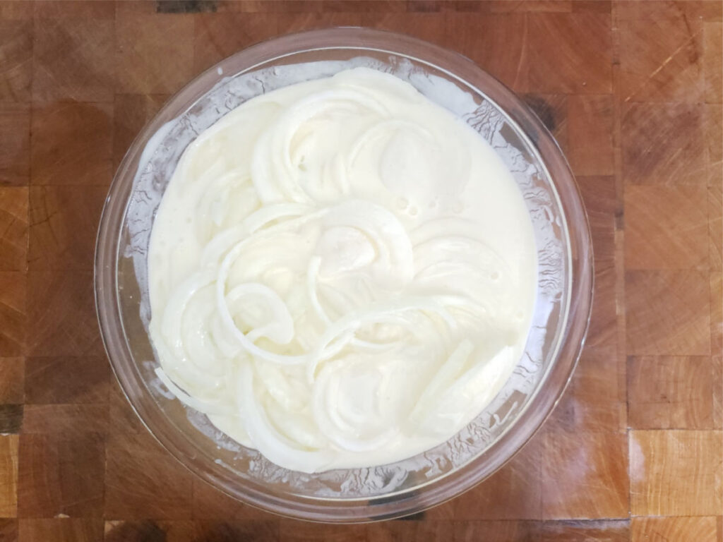 onion rings soaking in bowl of buttermilk on butcher block