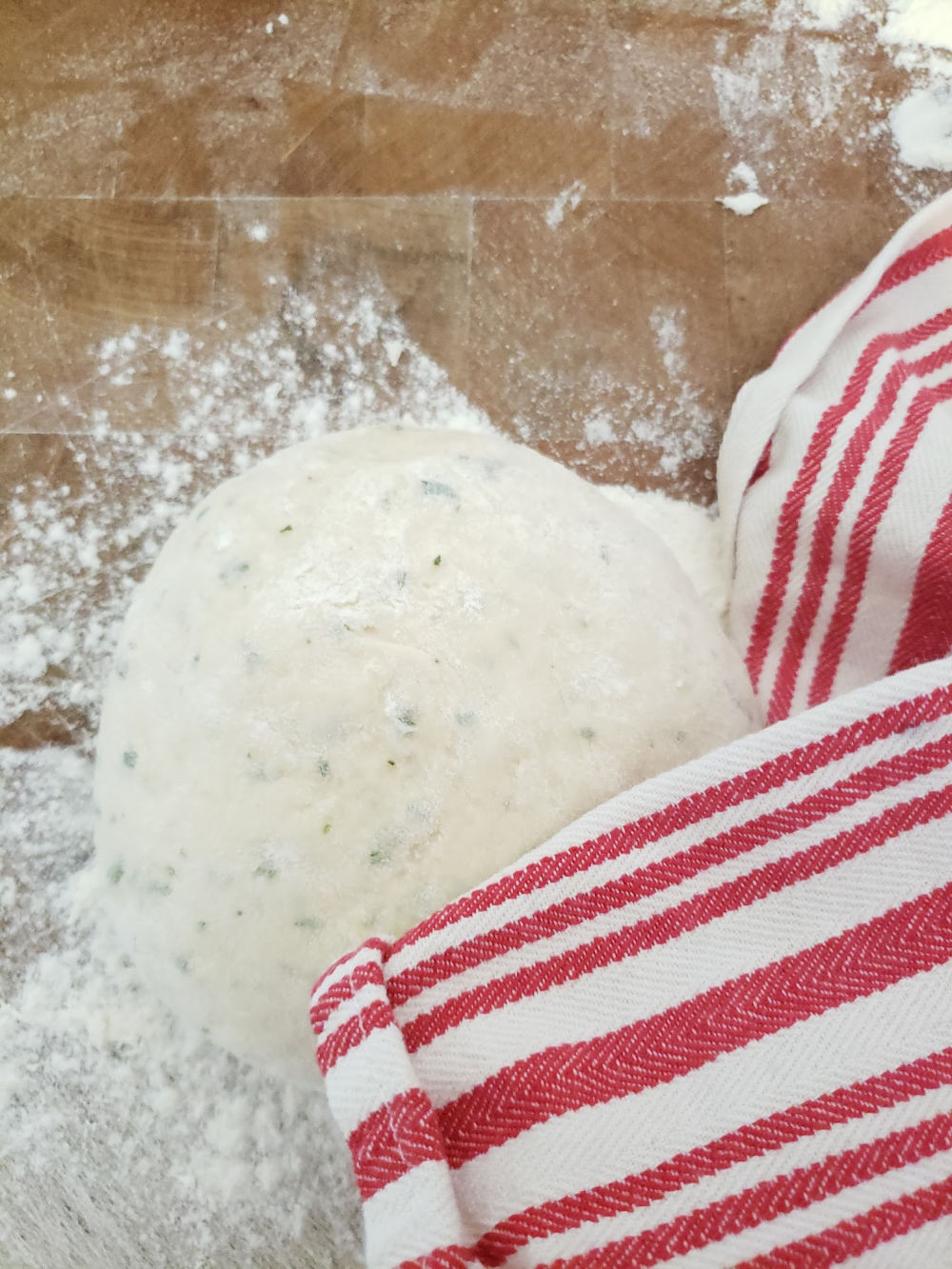 dinner roll dough rising on butcher block under red and white kitchen towel.