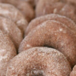 cider donuts lined up against each other on parchment lined half sheet pan