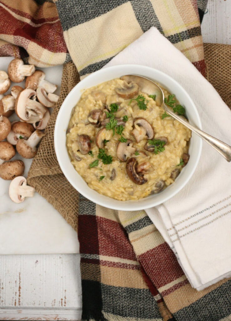 Mushroom risotto in a white bowl, with sauteed mushrooms and pieces of parsley