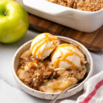 Small white bowl with apple crisp topped vanilla ice cream.