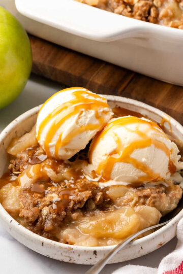 Small white bowl with apple crisp topped vanilla ice cream.