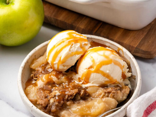 Small white bowl with apple crisp topped vanilla ice cream.