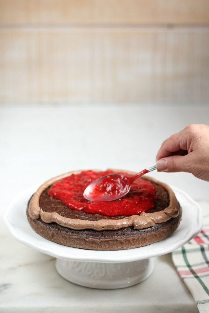 spreading raspberry filling on a chocolate layer cake