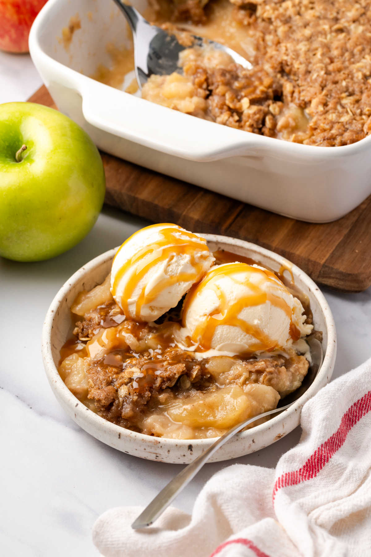 Apple crisp with scoops of vanilla ice cream in small white bowl.