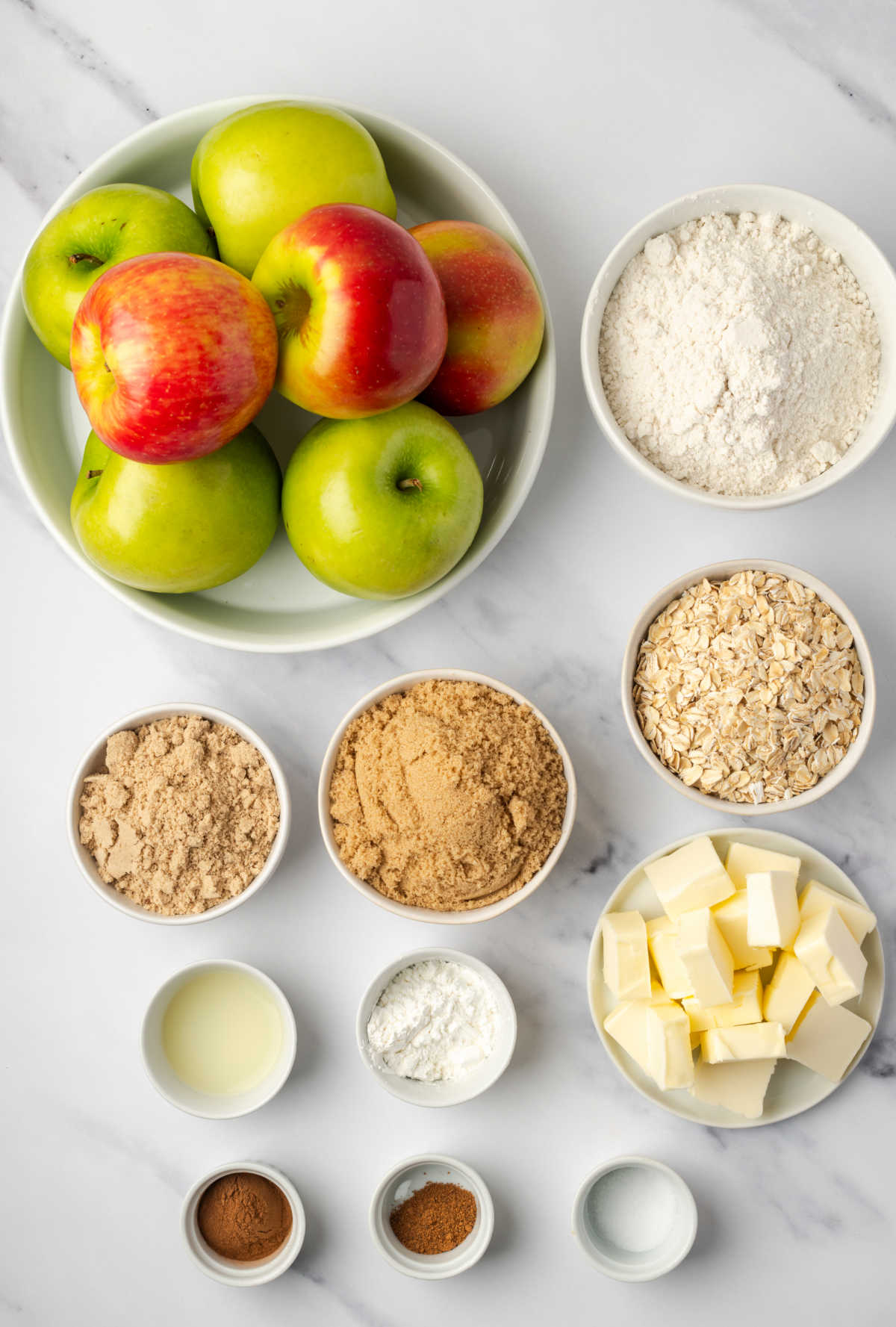Ingredients in small white bowls, apples in bowl for apple crisp.