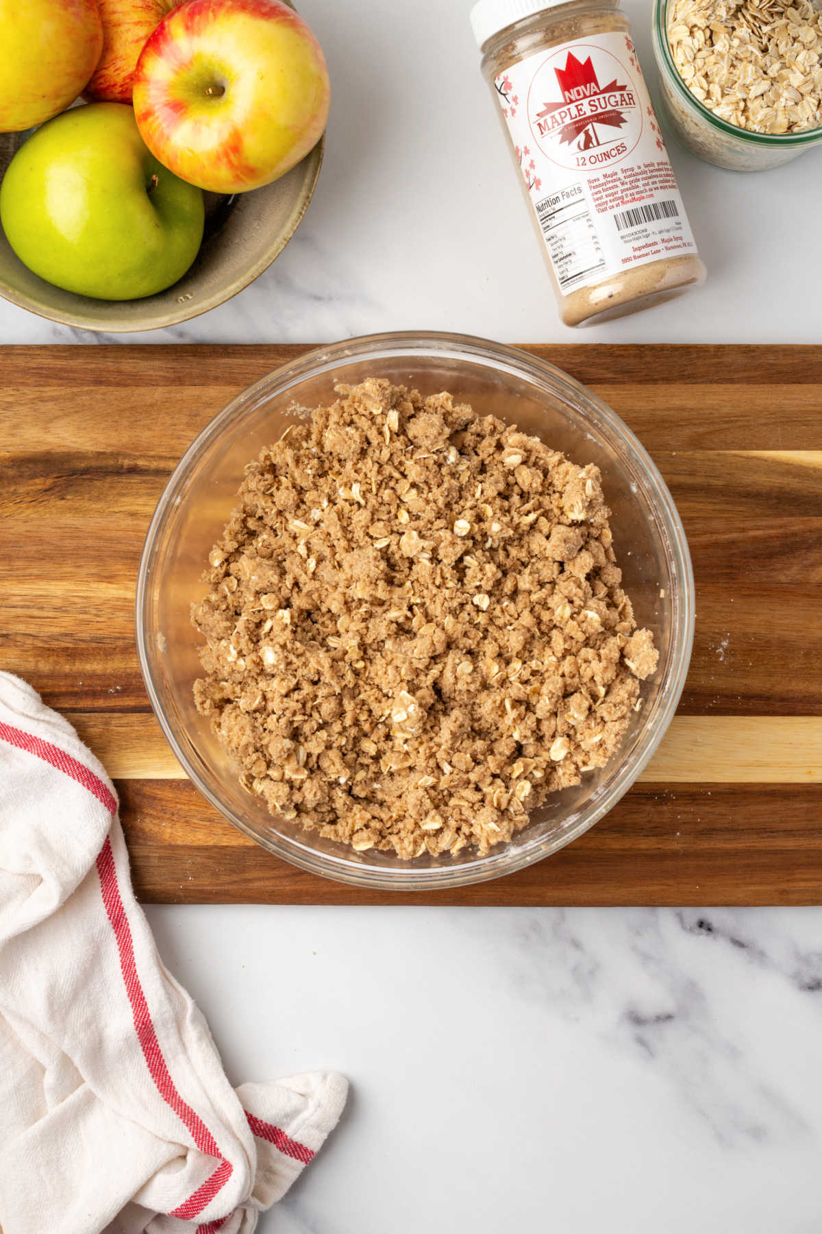 Oat crumb topping in clear glass bowl on wood cutting board.