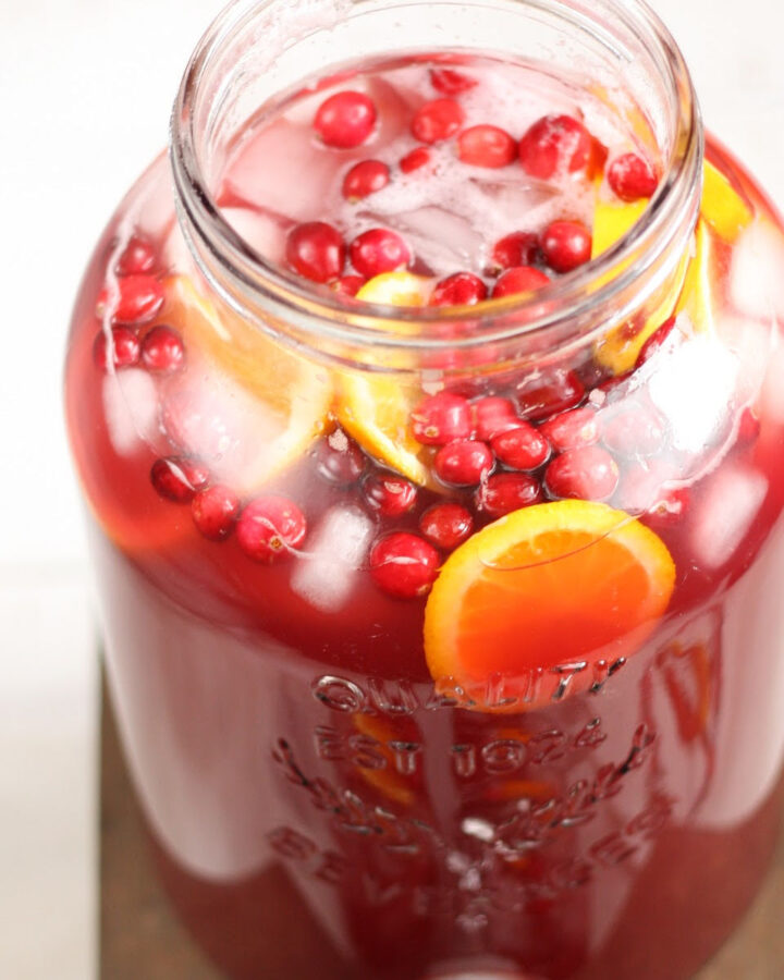 Glass pouring pitcher with holiday cranberry punch, cranberries and orange slices.
