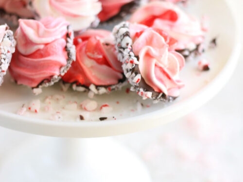 Pink and red swirled meringue cookies dipped in chocolate, rolled in crushed peppermints on glass footed cake dish