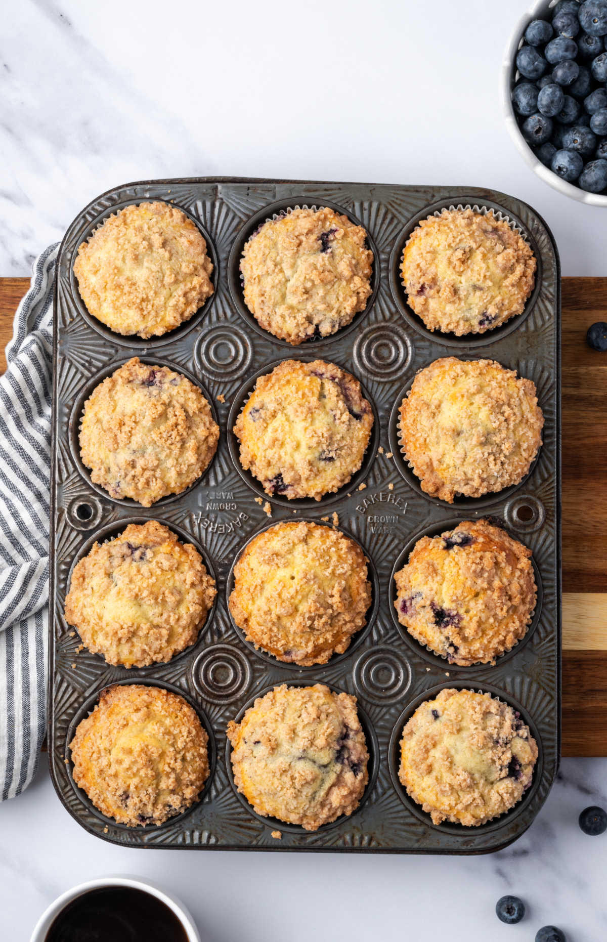 Blueberry muffins in vintage muffin tin, fresh blueberries in white bowl.