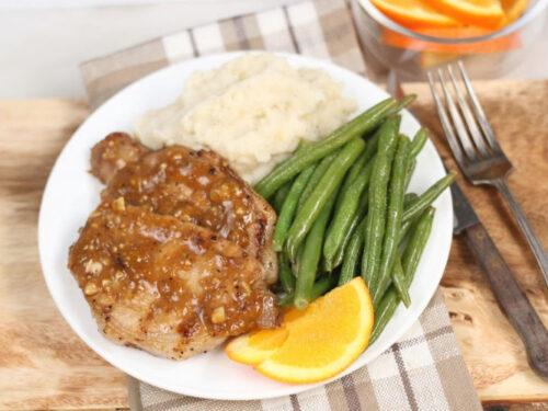 grilled pork chops on white plate with green beans, mashed potatoes, and slices of oranges
