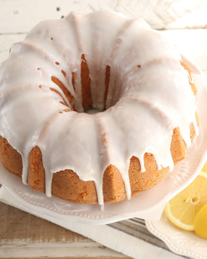 Bundt cake with lemon icing on white footed cake dish.