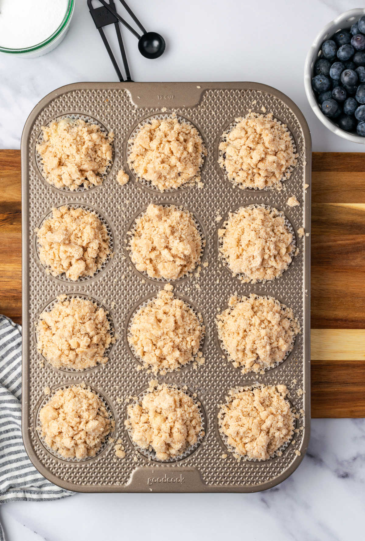 Unbaked muffins in muffin tin with crumb topping.