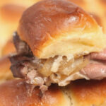 roast beef sliders with caramelized onions on sheet pan.