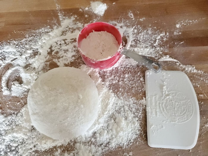 pizza dough shaped into round on floured butcher block