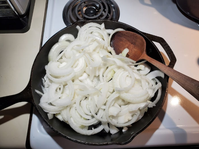 sliced onions cooking on stove in cast iron skillet