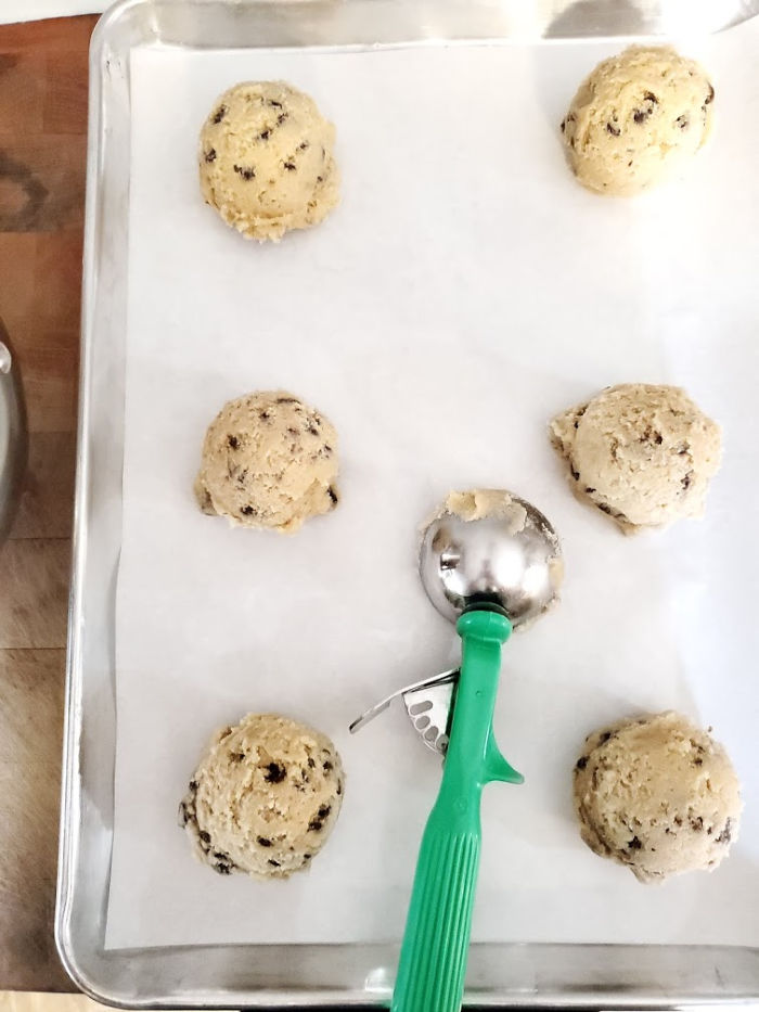 chocolate chip cookie dough scooped onto half sheet pan lined with parchment paper.
