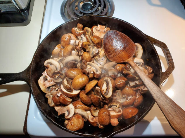browning mushrooms in cast iron skillet, wooden spoon in pan
