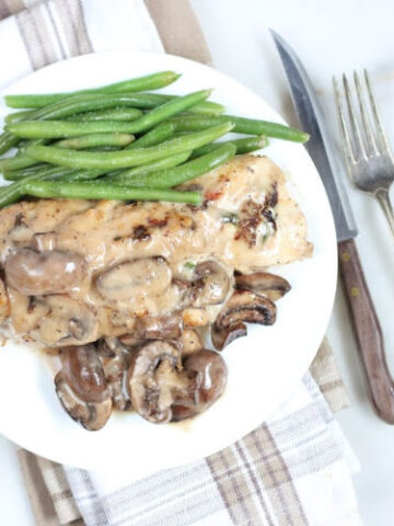spinach stuffed chicken breast with mushrooms and cream sauce on white plate with fresh green beans