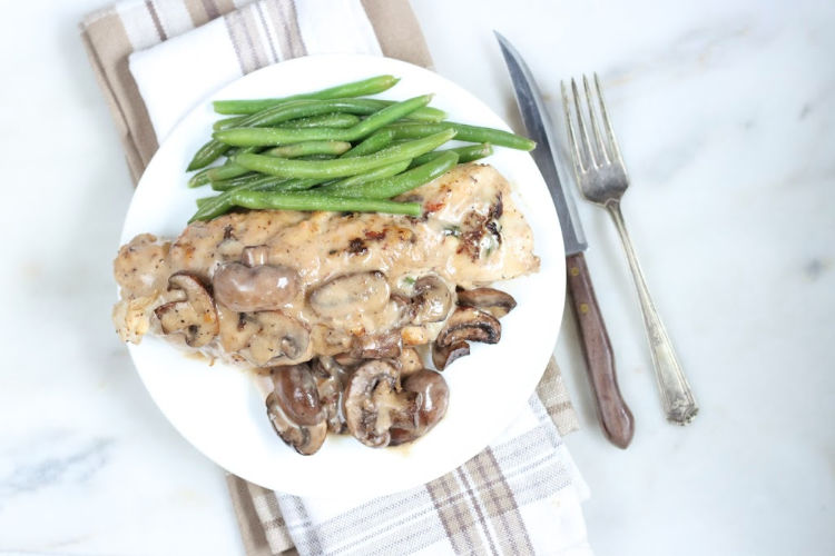 spinach stuffed chicken breast with mushrooms and cream sauce on white plate with fresh green beans